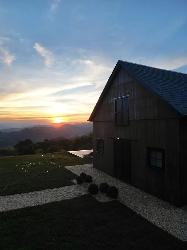 O celeiro da Felix Hills Barn em silhueta, com o sol se pondo atrás dos morros